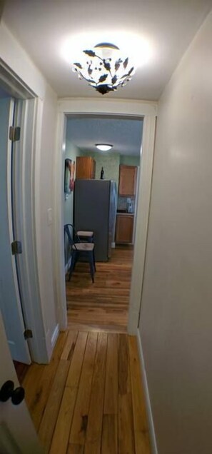 A narrow hallway with wooden flooring, a ceiling light fixture, and a door on the left. - Harper, Two Bedroom House in Historic Loveland (Loveland)