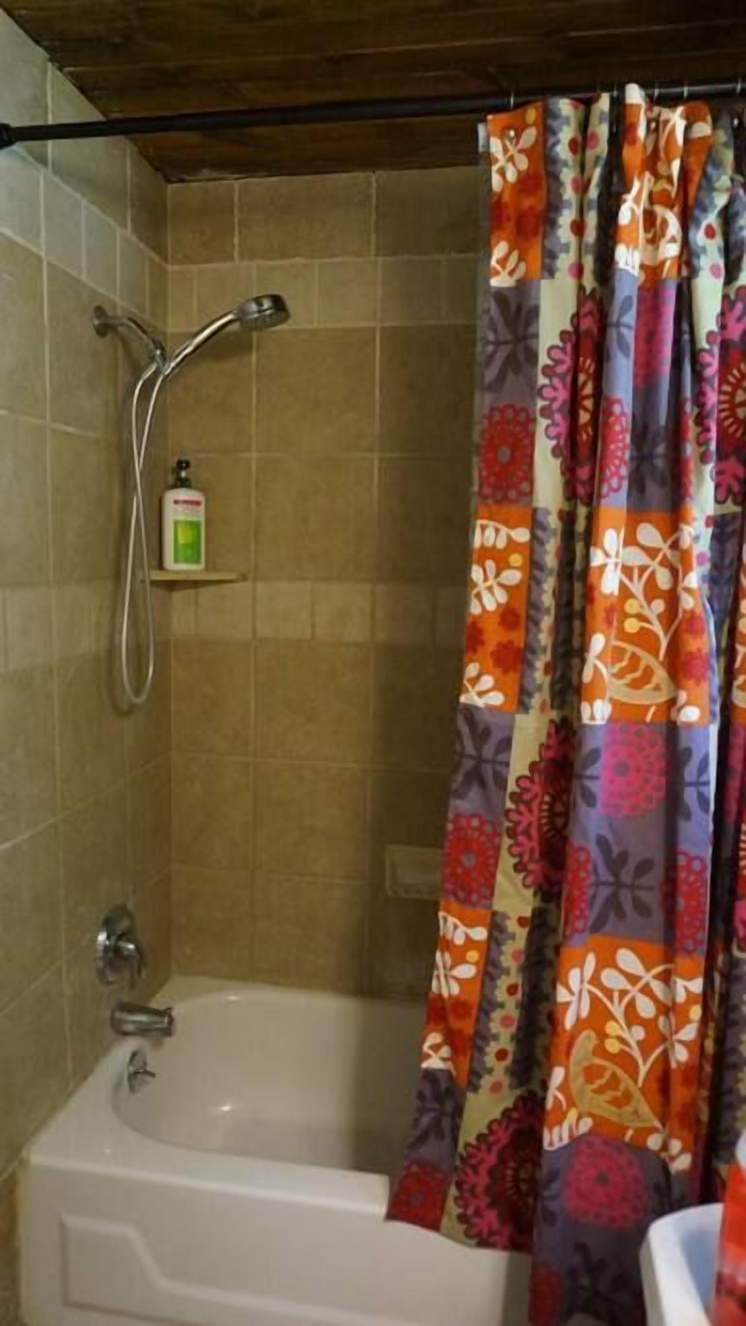 Bagno con vasca, doccia e uno scaffale con una bottiglia.