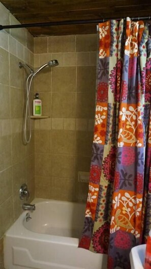 A bathroom with a bathtub, shower, and a shelf with a bottle. - Harper, Two Bedroom House in Historic Loveland (Loveland)