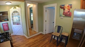 A kitchen with wooden flooring, a refrigerator, a chair, and a door leading to another room.