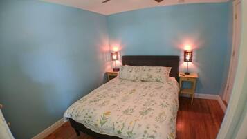 Un dormitorio con cama, dos lámparas de noche, ventilador de techo y suelo de madera.