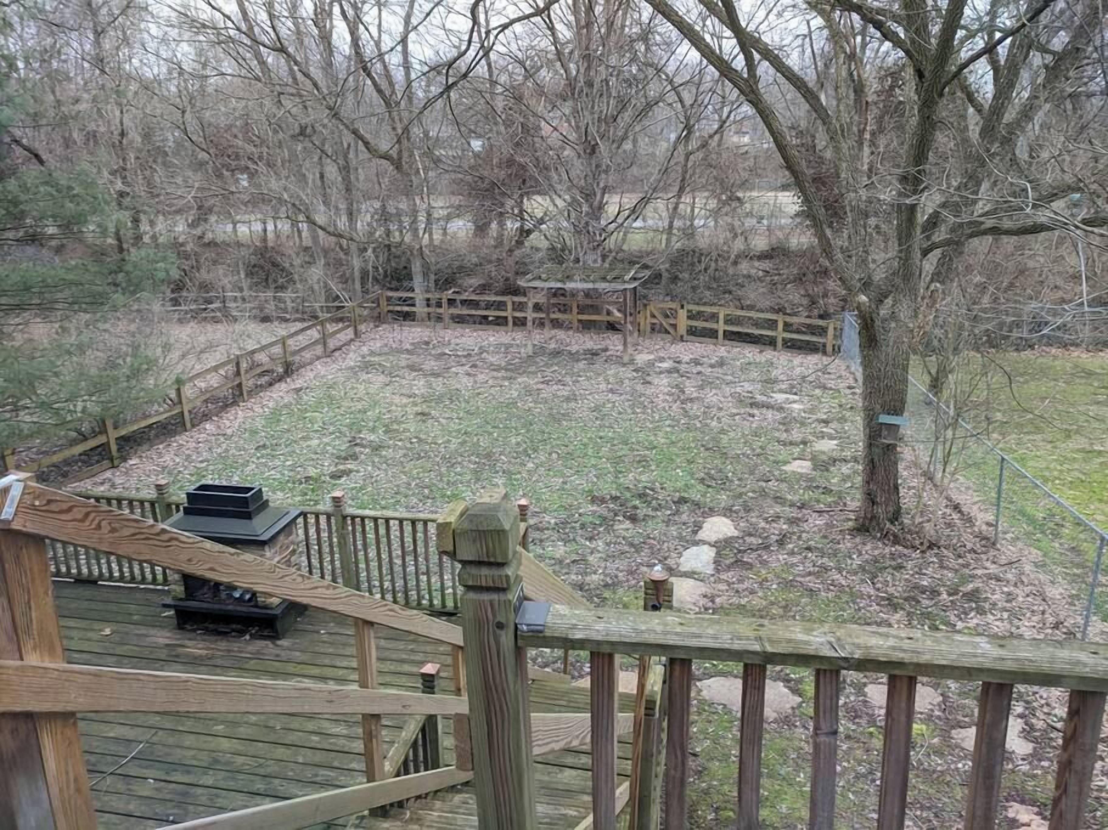 A wooden deck with a metal railing, a bench, and a tree in the background.