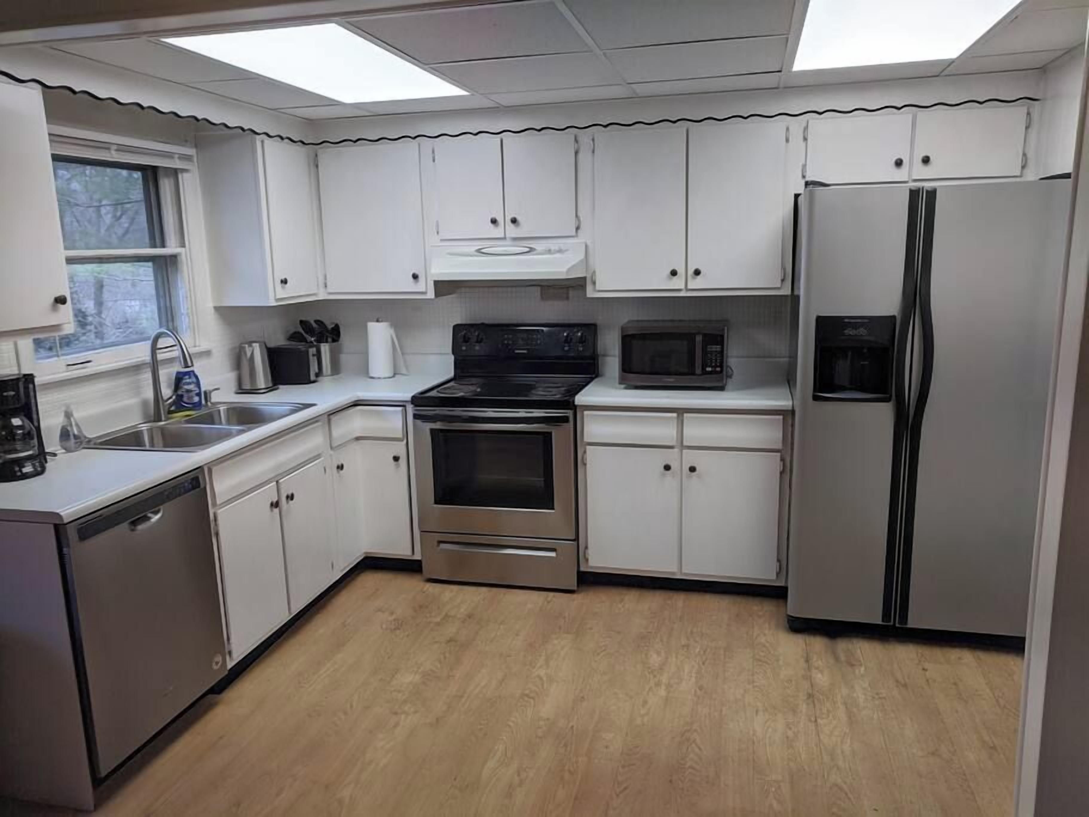 A modern kitchen with stainless steel appliances, white cabinets, and a wooden floor.