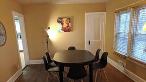 A dining area with a round table and six chairs, a painting on the wall, a door, and a window with blinds. - Ohio Ave, 3 bed house, Historic Downtown Loveland (Loveland)