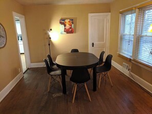 A dining area with a round table and six chairs, a painting on the wall, a door, and a window with blinds. - Ohio Ave, 3 bed house, Historic Downtown Loveland (Loveland)