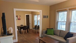A living room with a sofa, a coffee table, a dining table with chairs, and a TV on a stand. - Ohio Ave, 3 bed house, Historic Downtown Loveland (Loveland)