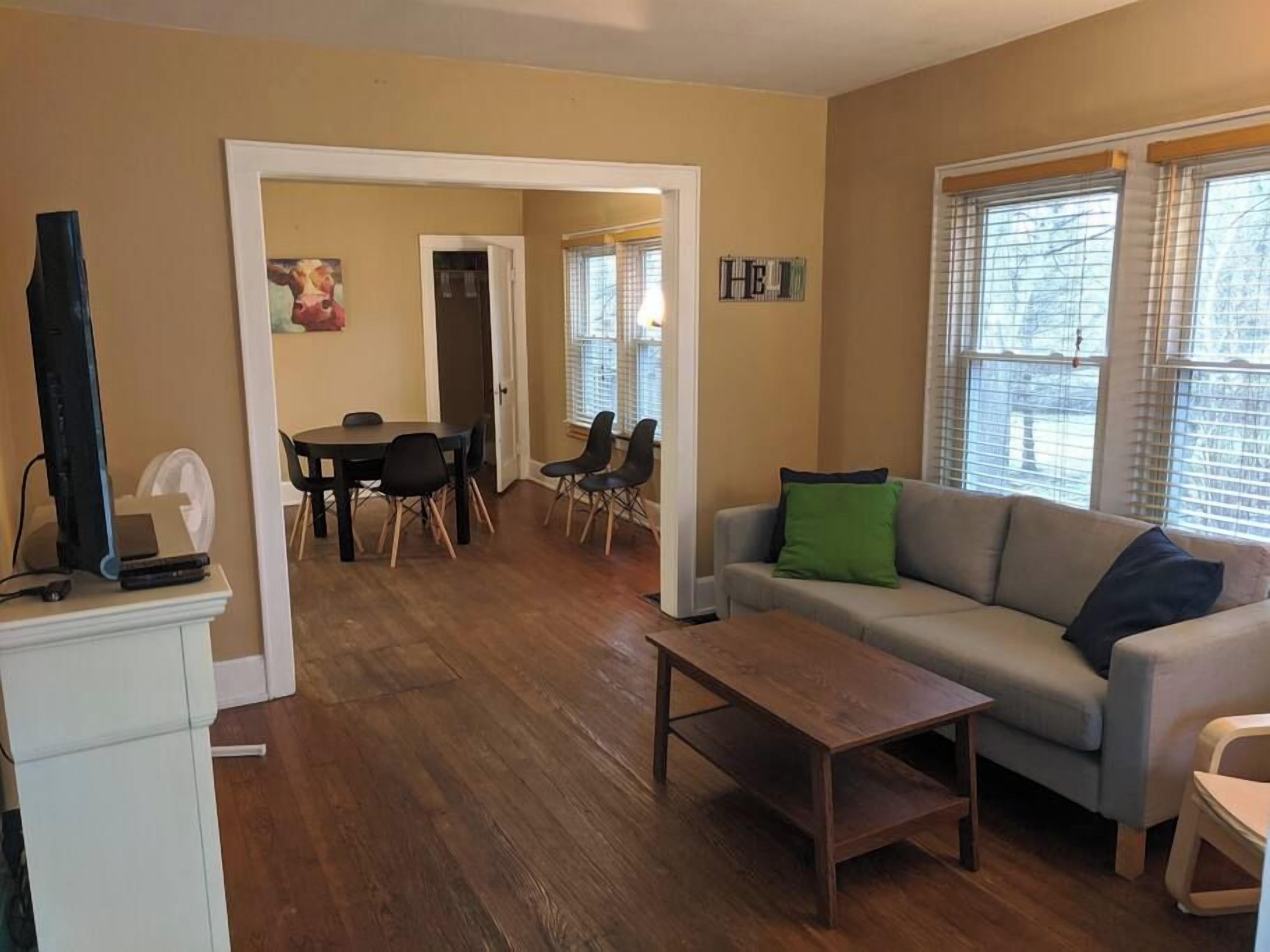 A living room with a sofa, a coffee table, a dining table with chairs, and a TV on a stand.
