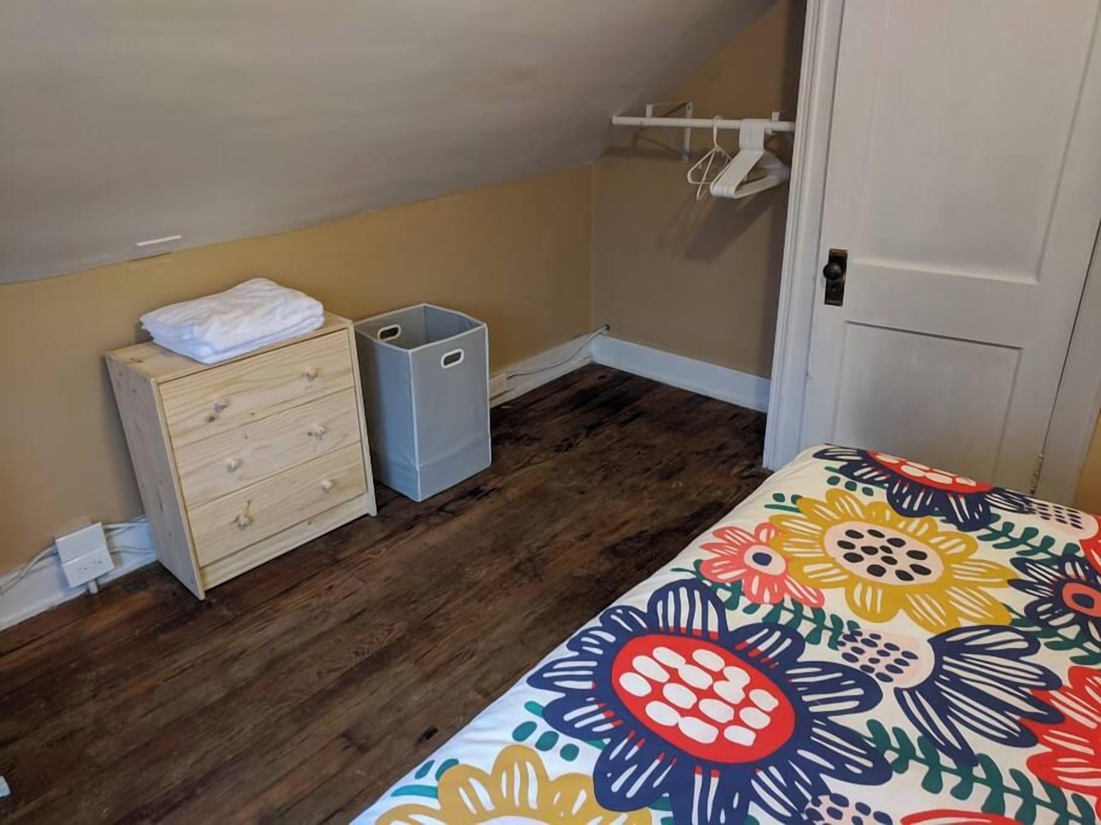 A bedroom with a wooden dresser, two gray storage bins, a colorful floral bedspread, and a white door.