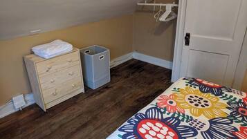 A bedroom with a wooden dresser, two gray storage bins, a colorful floral bedspread, and a white door.