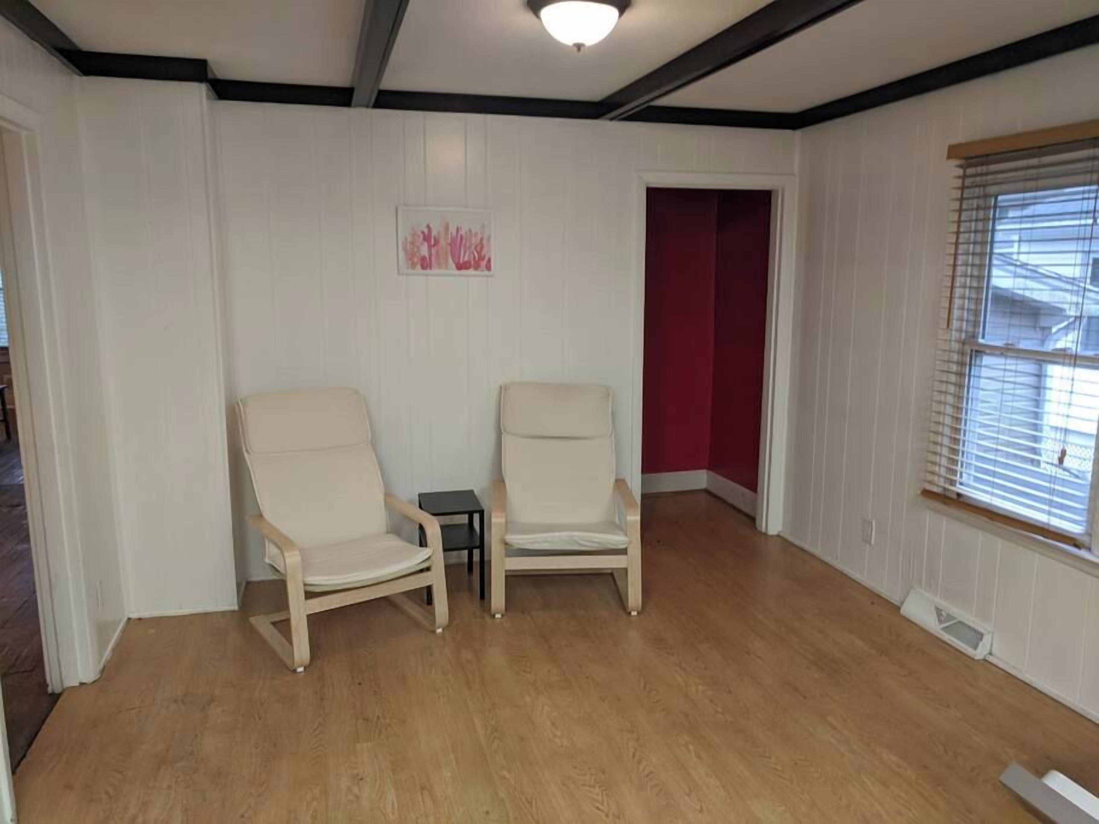 Quarto com duas poltronas bege, uma mesa pequena e uma parede de destaque vermelha.