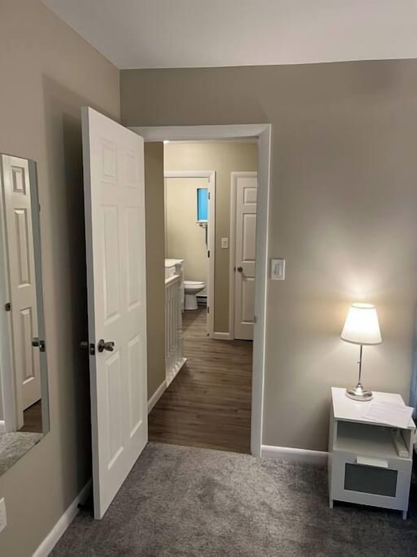 A hallway with a carpeted floor, white walls, and a door leading to a bathroom.