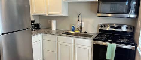 Una cocina con armarios blancos, un refrigerador de acero inoxidable, un microondas y una estufa.