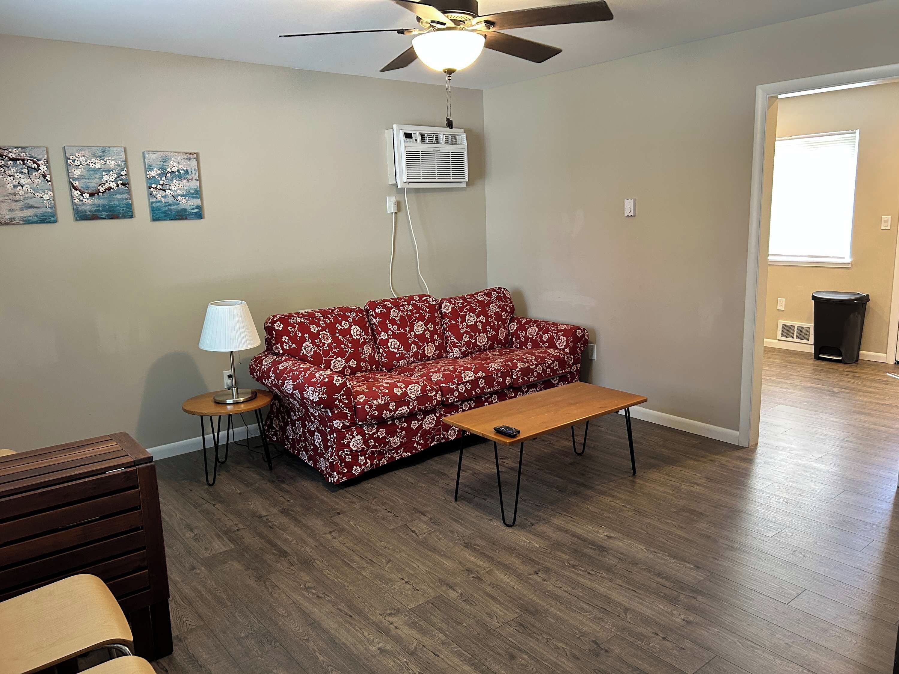A living room with a red floral sofa, a wooden coffee table, a lamp, and a ceiling fan.