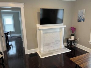 A modern living room with a fireplace, a flat-screen TV mounted above it, and a small table with a potted plant. - Ridgeway, 2 Bedroom House near Xavier, Downtown (Cincinnati)