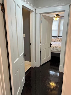 A narrow hallway with white doors leading to a bedroom with a bed and a ceiling fan. - Ridgeway, 2 Bedroom House near Xavier, Downtown (Cincinnati)