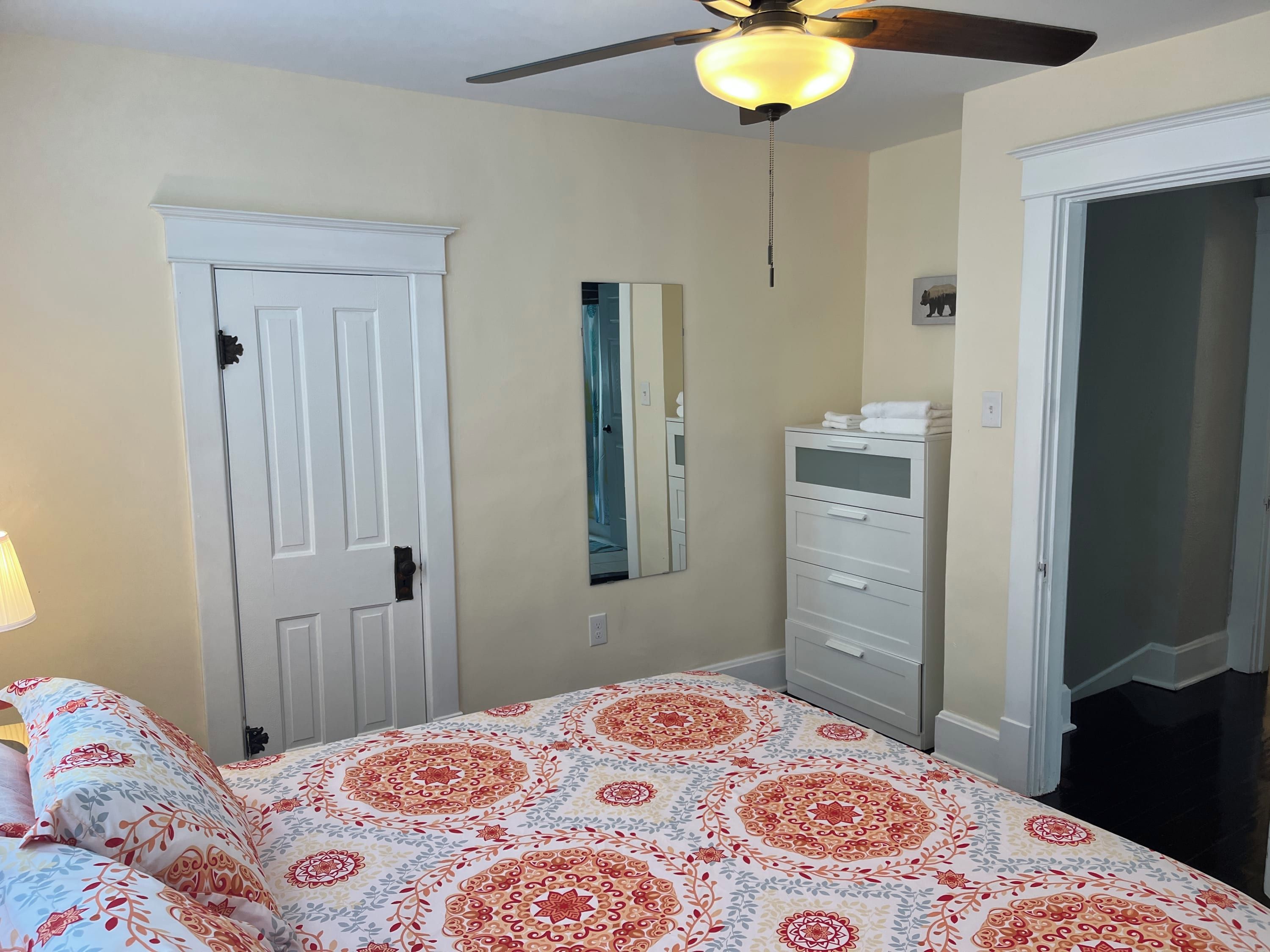 A bedroom with a bed, a ceiling fan, a dresser, and a door.