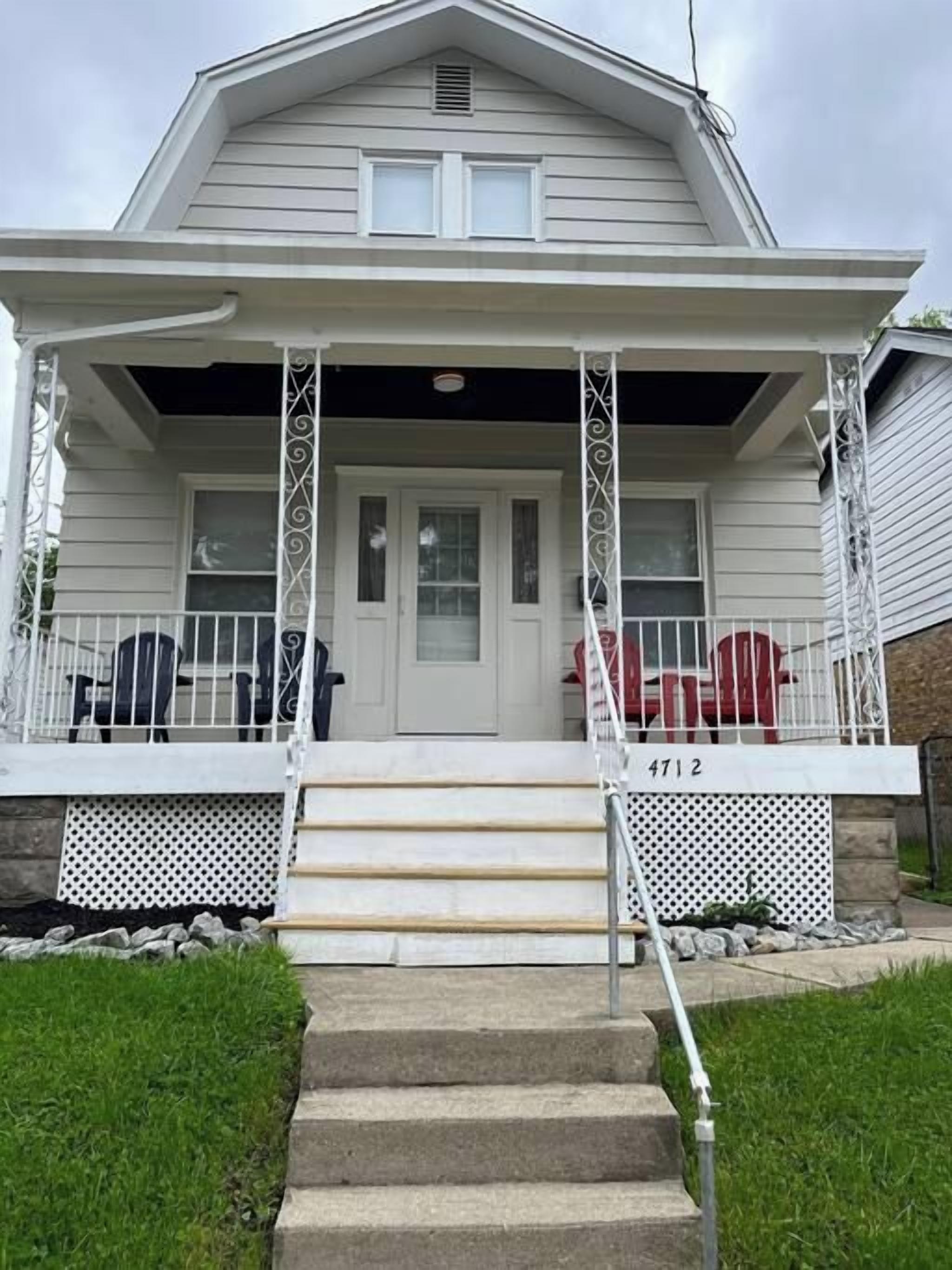 Une maison à deux étages avec un porche à l’avant, une porte d’entrée et un escalier menant à l’entrée.