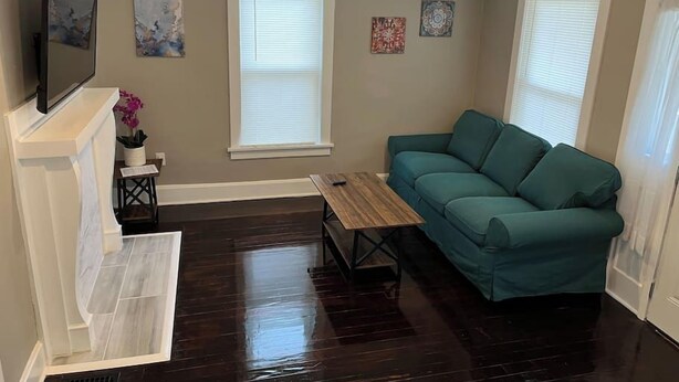 A living room with a green sofa, a wooden coffee table, a fireplace, and artwork on the walls. - Ridgeway, 2 Bedroom House near Xavier, Downtown (Cincinnati)