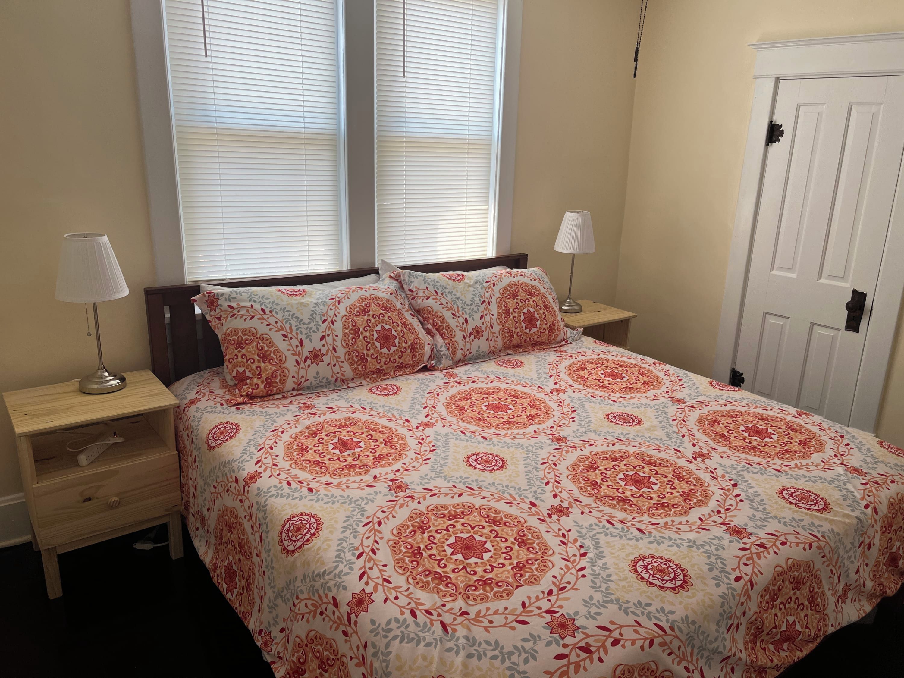 A bedroom with a bed, two bedside tables, a nightstand, a lamp, and a door.