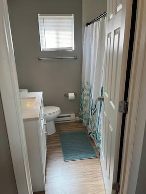 A narrow bathroom with a toilet, a towel rack, and a shower curtain.