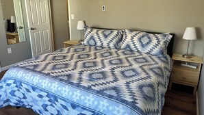 A bed with a patterned bedspread, two bedside lamps, a nightstand, and a mirror on the wall.