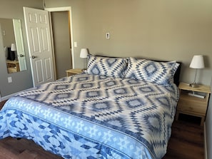 A bed with a patterned bedspread, two bedside lamps, a nightstand, and a mirror on the wall.