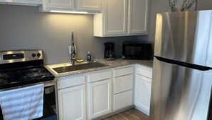 A kitchen with white cabinets, a stainless steel refrigerator, a microwave, a stove, and a sink.