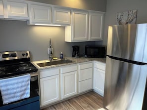 A kitchen with white cabinets, a stainless steel refrigerator, a microwave, a stove, and a sink.