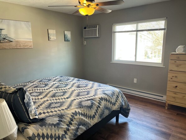 A bedroom with a bed, a ceiling fan, a window, and a dresser.