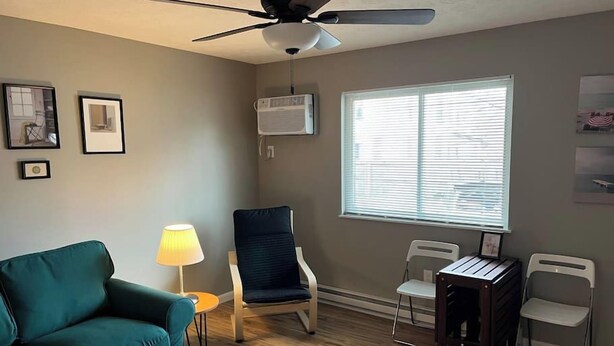 A living room with a teal sofa, a ceiling fan, a window with blinds, and a small table with a lamp.