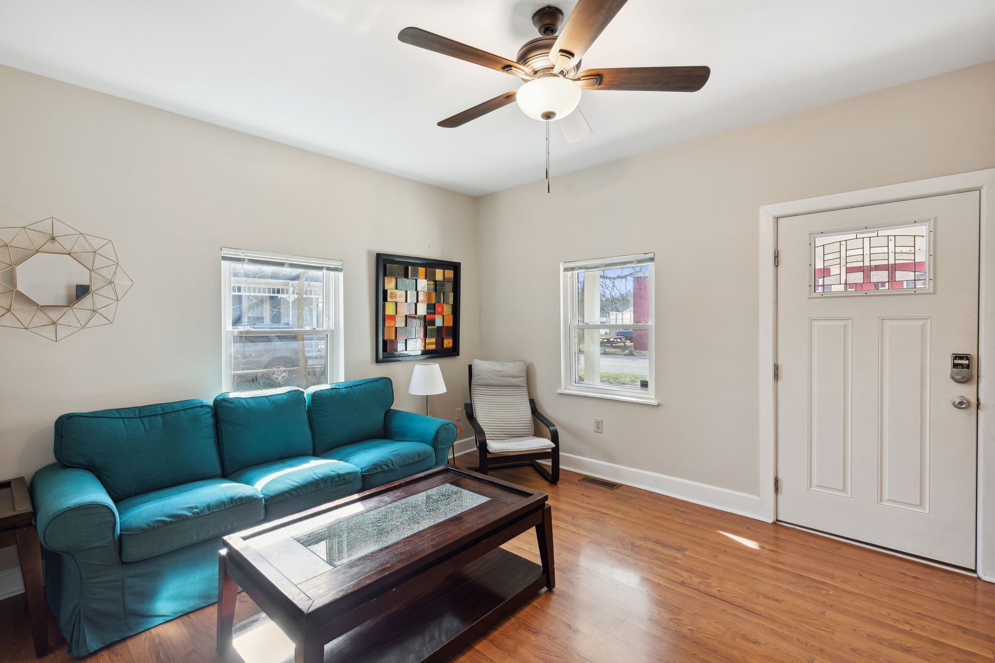 A living room with a teal sofa, a wooden coffee table, a ceiling fan, and a door with a window.