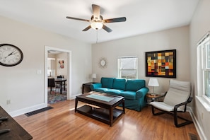 A living room with a teal sofa, a wooden coffee table, a ceiling fan, and a wall clock. - Chestnut, Three Bedroom House in Historic Loveland (Loveland)