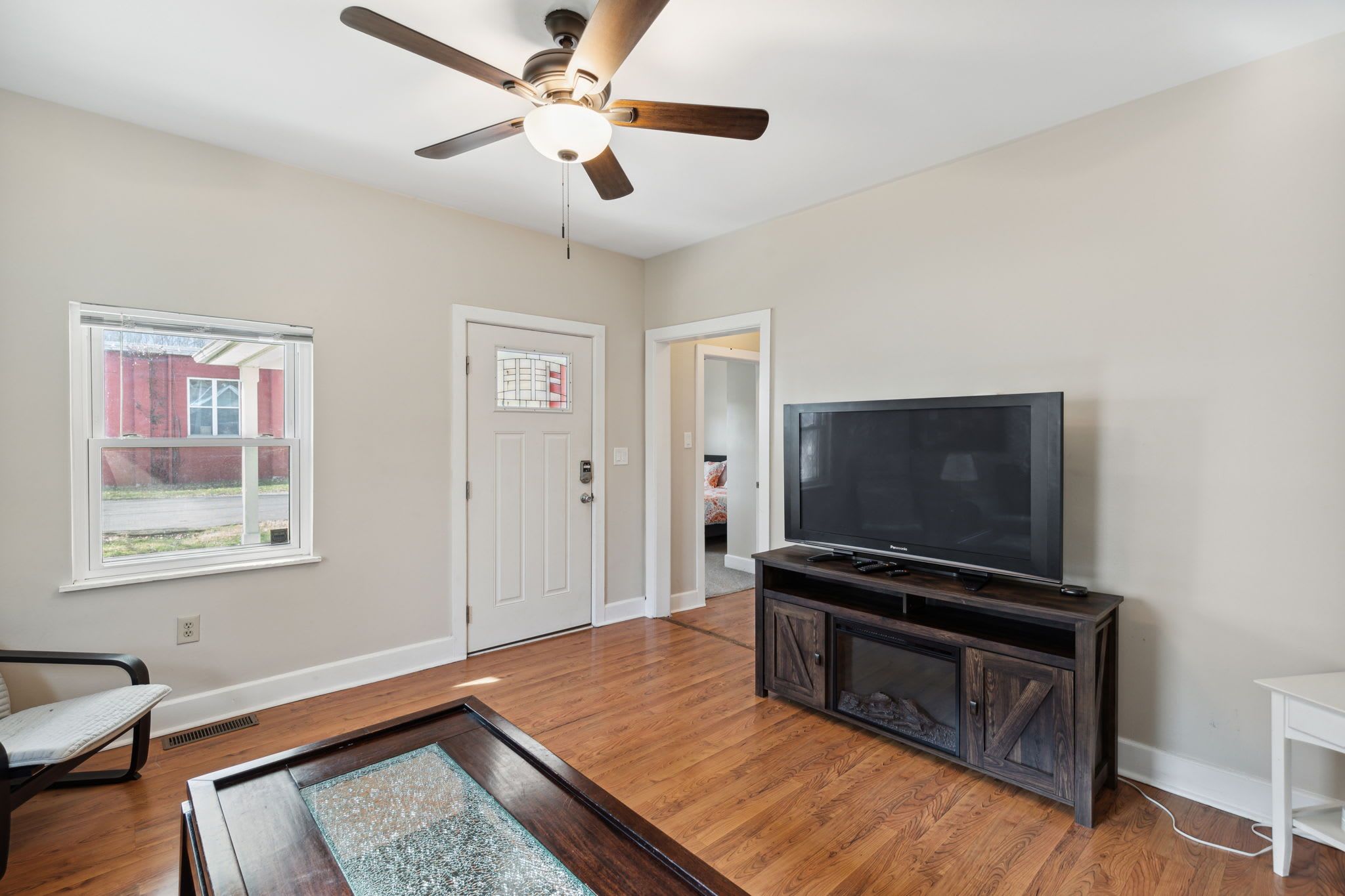 A spacious living room with hardwood flooring, a ceiling fan, a large flat-screen TV, and a wooden entertainment center.