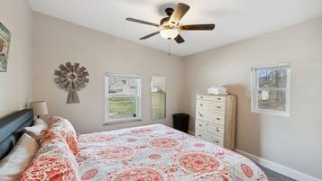 A bedroom with a bed, a ceiling fan, a dresser, a mirror, and two windows.