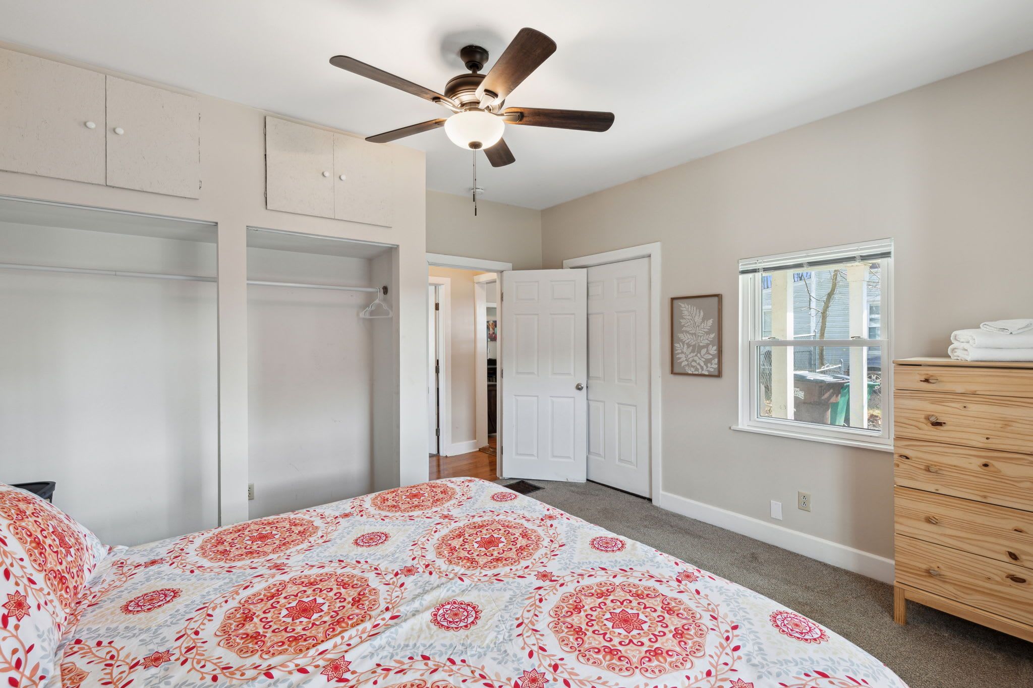 A bedroom with a bed, a ceiling fan, a dresser, and a window.