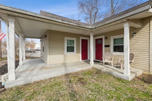 A two-story house with a covered porch, a red door, and a small outdoor seating area. - Chestnut, Three Bedroom House in Historic Loveland (Loveland)