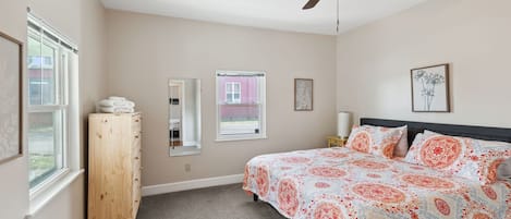A bedroom with a bed, a ceiling fan, a dresser, and two windows.