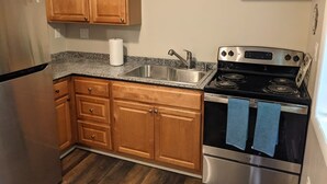 A kitchen with wooden cabinets, a stainless steel refrigerator, a granite countertop, a sink, and a black stove with blue towels.