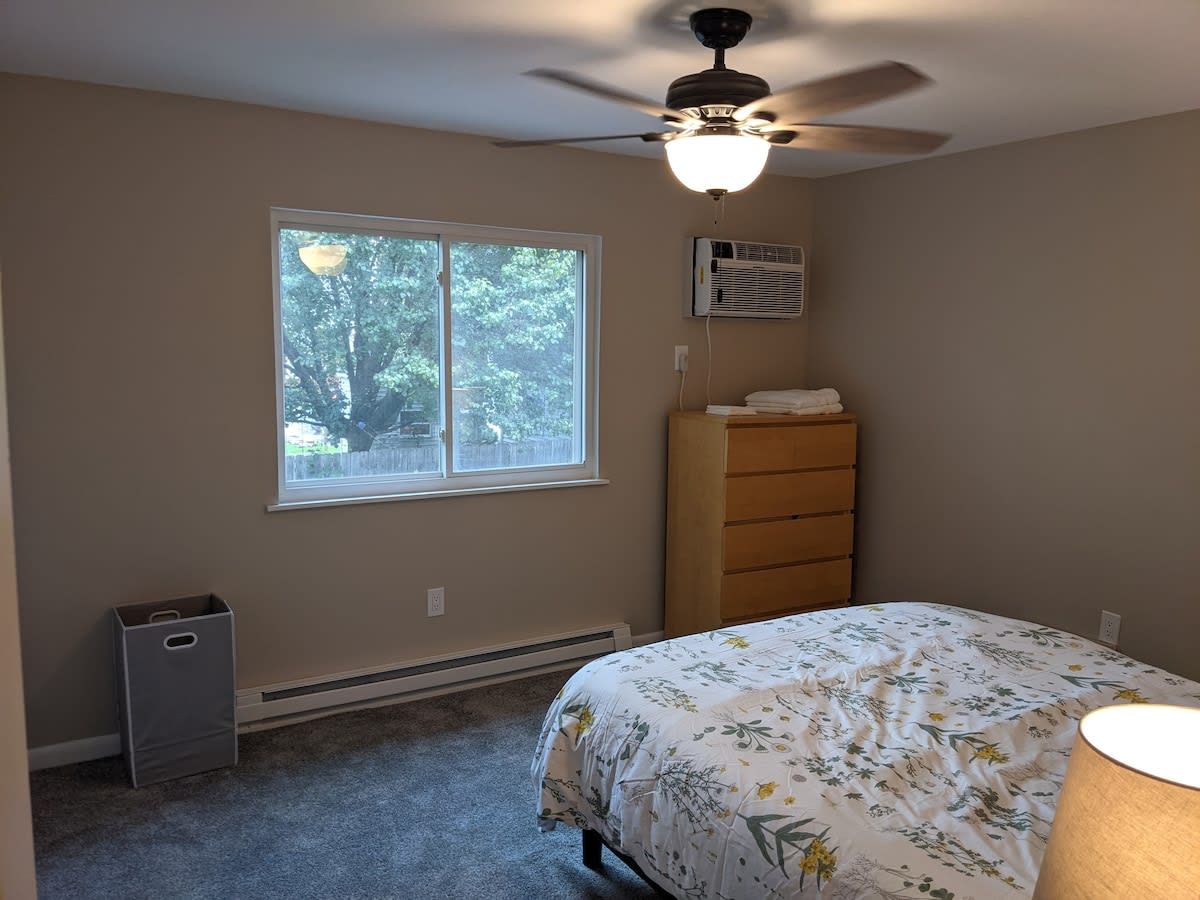 Un dormitorio con cama, cómoda, ventana, ventilador de techo y calefactor.