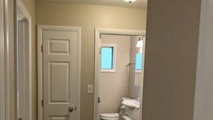 A narrow hallway with a wooden floor, a white door, and a bathroom visible in the background.