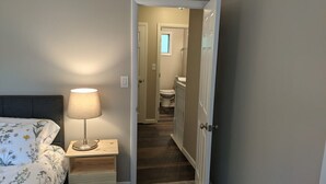 A bedroom with a bed, bedside table with a lamp, and a door leading to a bathroom.