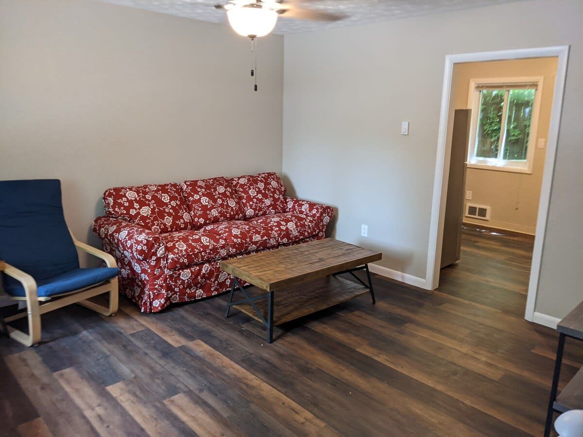 Une pièce avec un plancher en bois, un canapé à motifs floraux rouges, une chaise bleue et une table basse en bois.