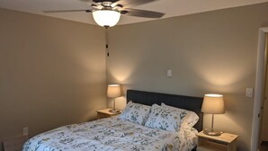 A bedroom with a bed, two bedside tables, a ceiling fan, and a nightstand with a lamp.