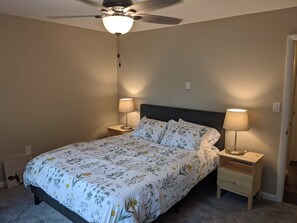 Une chambre à coucher comprenant un lit, deux tables de chevet, un ventilateur de plafond et une petite table de nuit avec une lampe.