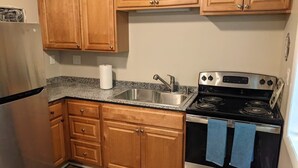 A kitchen with wooden cabinets, a stainless steel refrigerator, a granite countertop, a sink, and a black stove with blue towels. - Carter #5, Private Two Bed near Xavier, Downtown (Cincinnati)