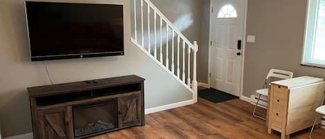 A living room with a flat-screen TV, wooden entertainment unit, staircase, and a small table with a document.