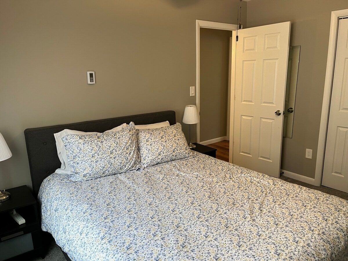 A bedroom with a bed, a nightstand, a lamp, and a door.
