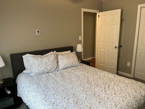 A bedroom with a bed, a nightstand, a lamp, and a door.