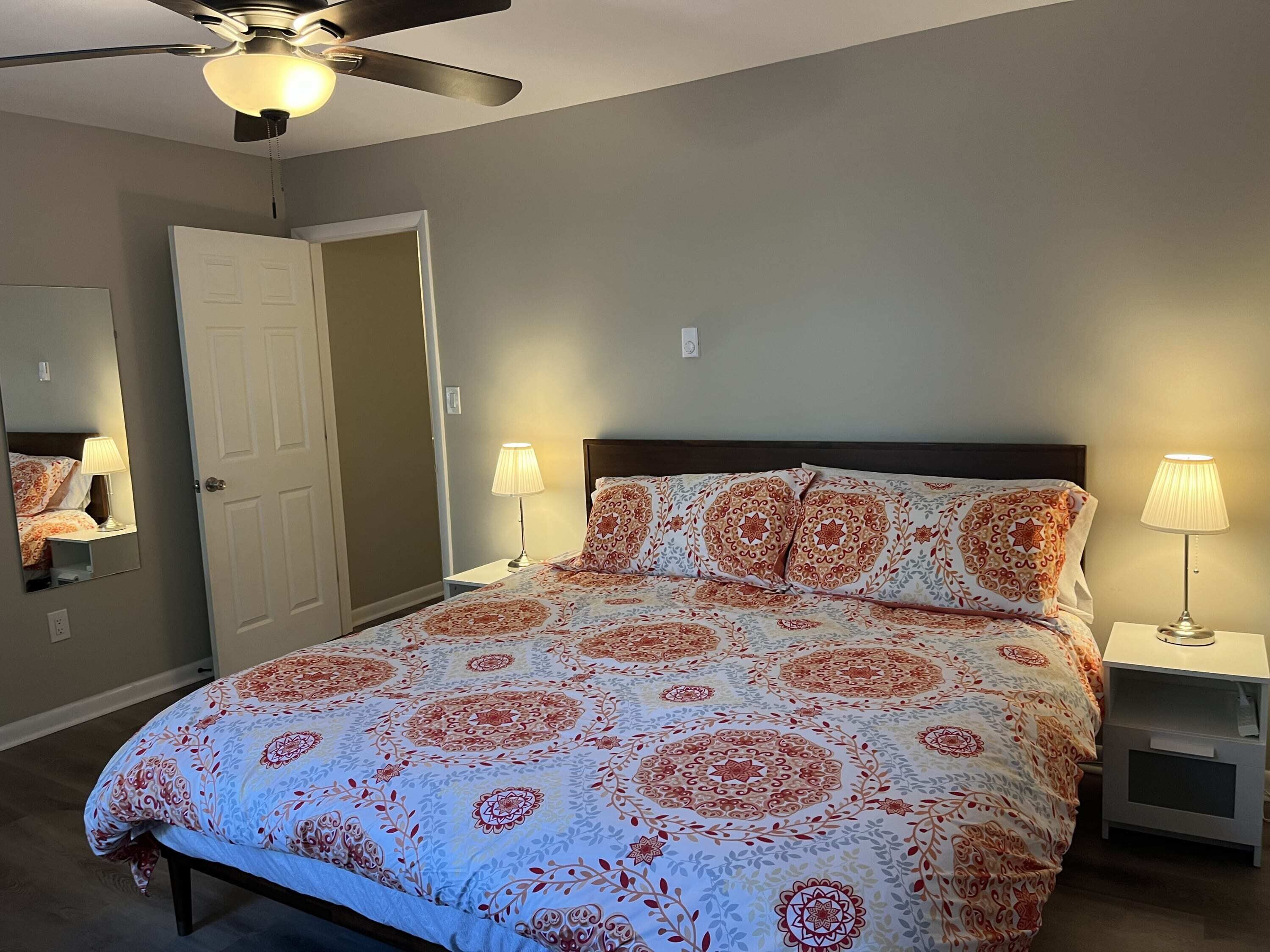 A bedroom with a bed, two bedside lamps, a ceiling fan, and a door.