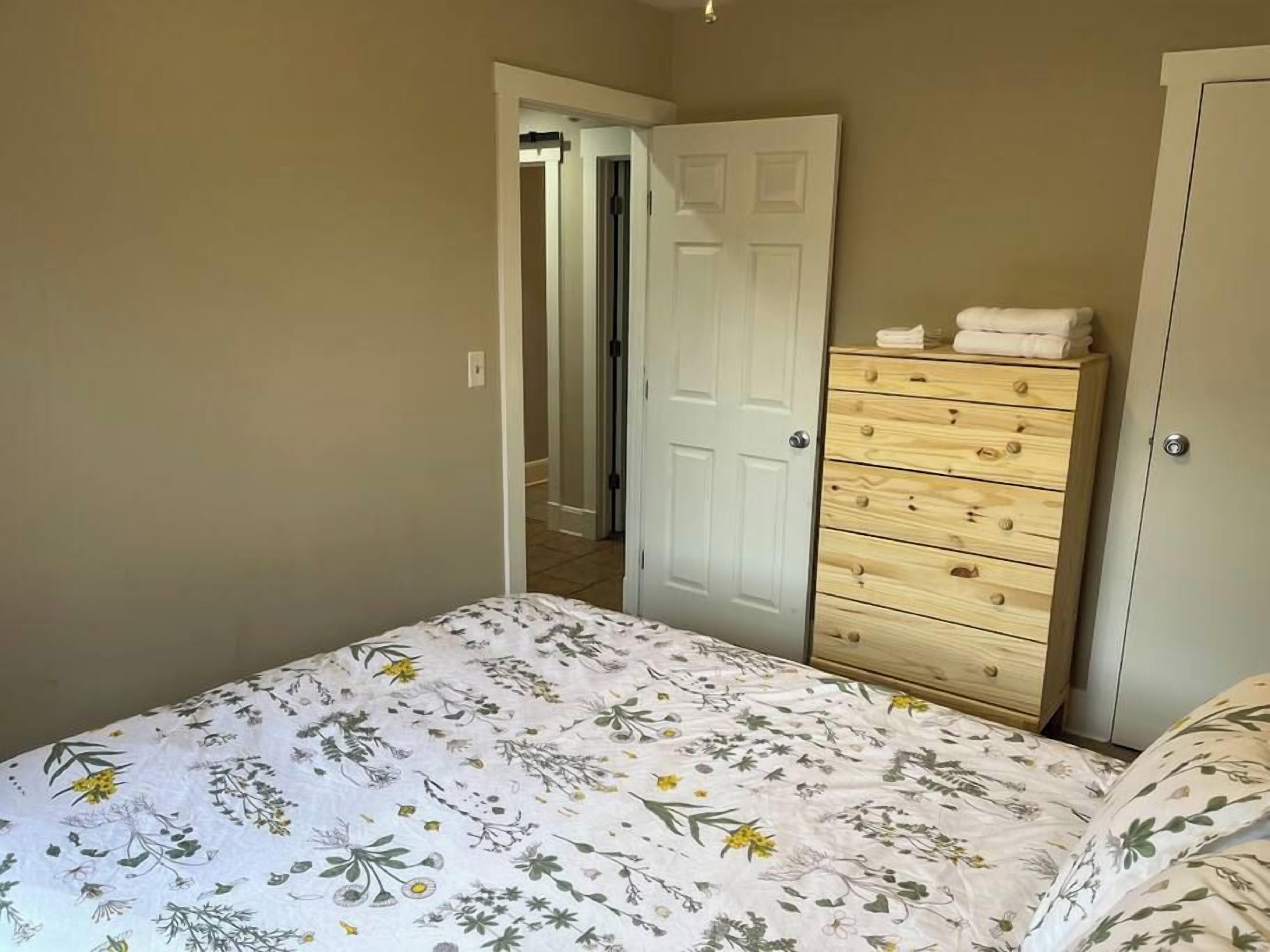 Quarto com uma cama, cômoda de madeira e porta que dá para outro ambiente.